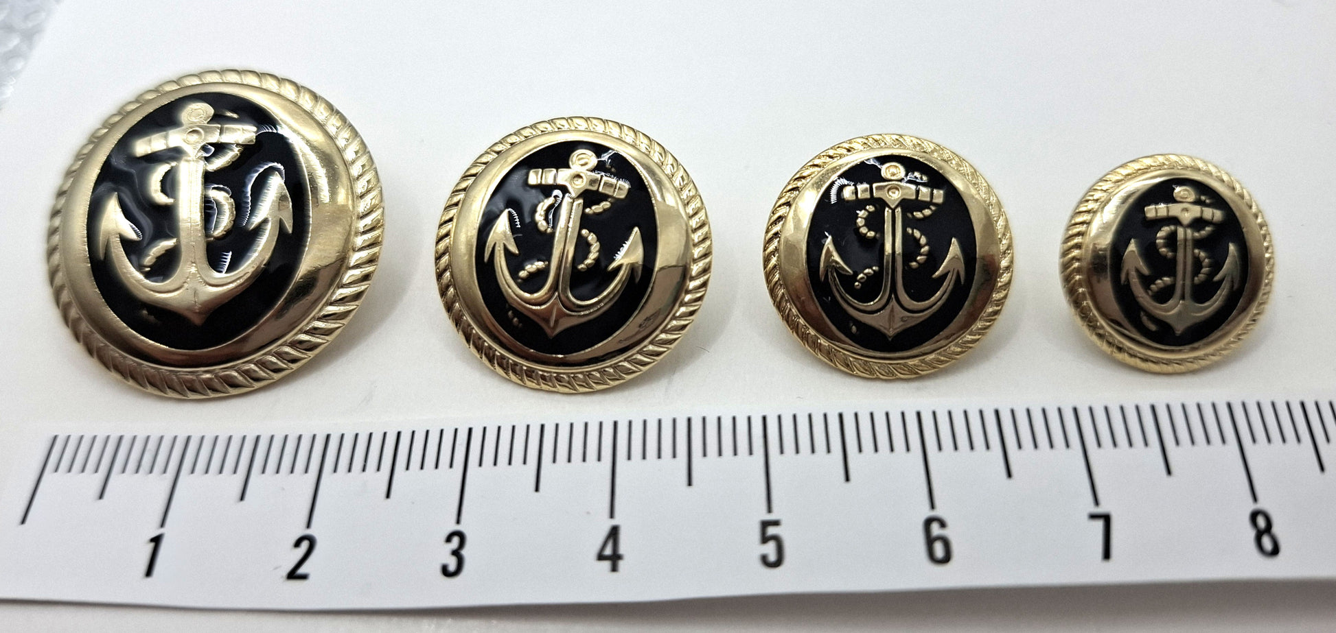 Set of four black and gold anchor buttons with a ruler for scale on a white background