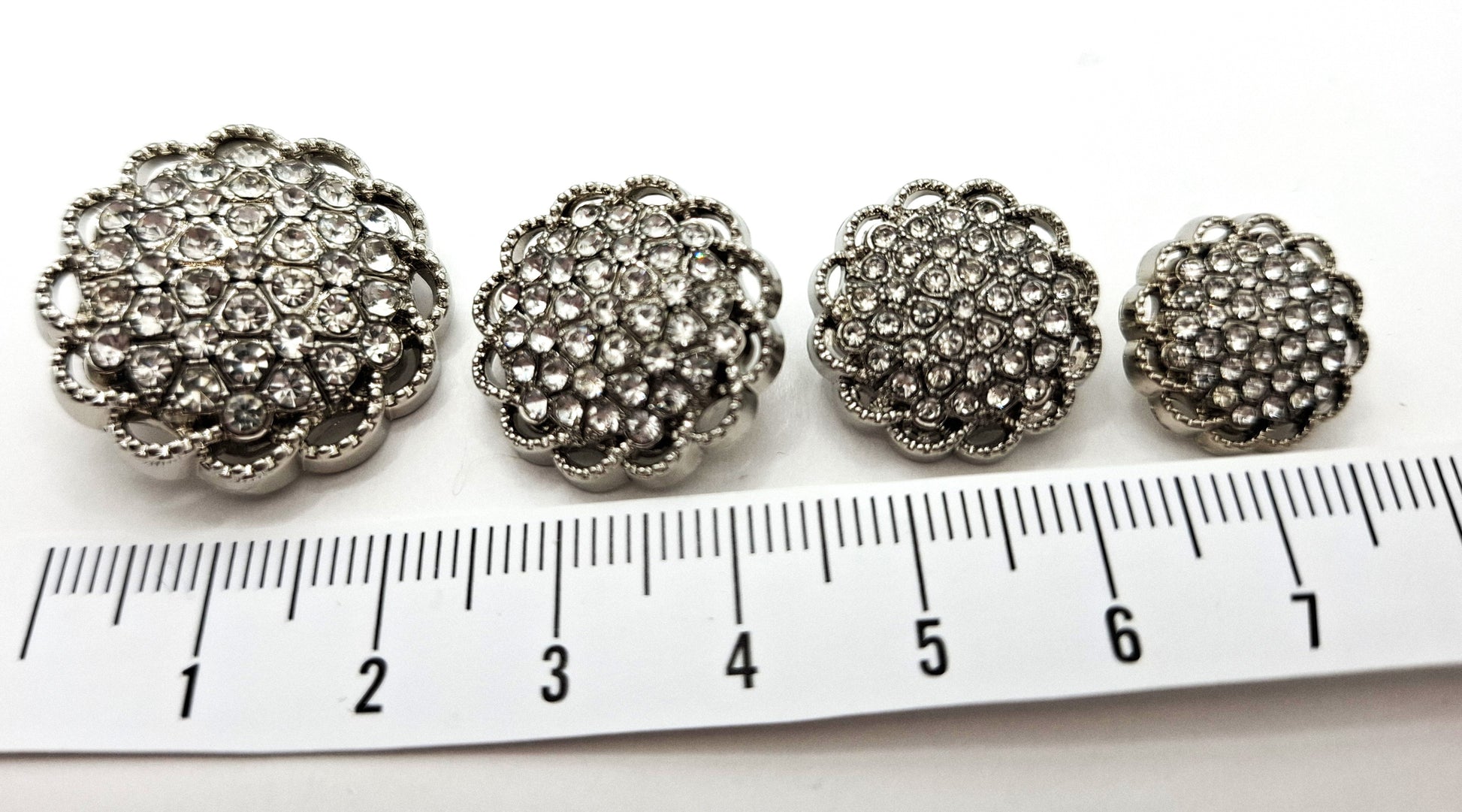 Four decorative buttons with rhinestones on a ruler for scale.